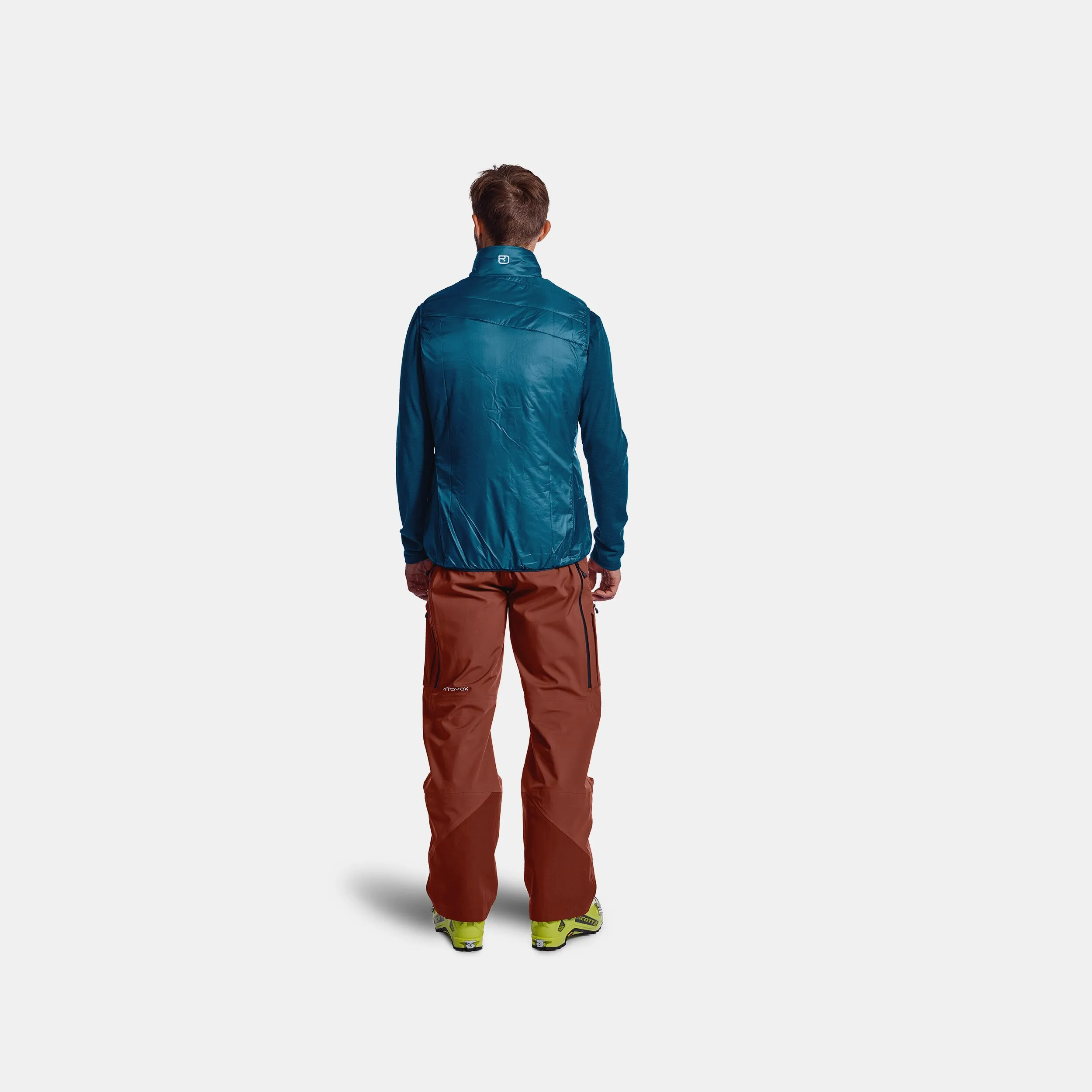 Man from behind, wearing blue PIZ Cartas vest and red pants, ski boots.