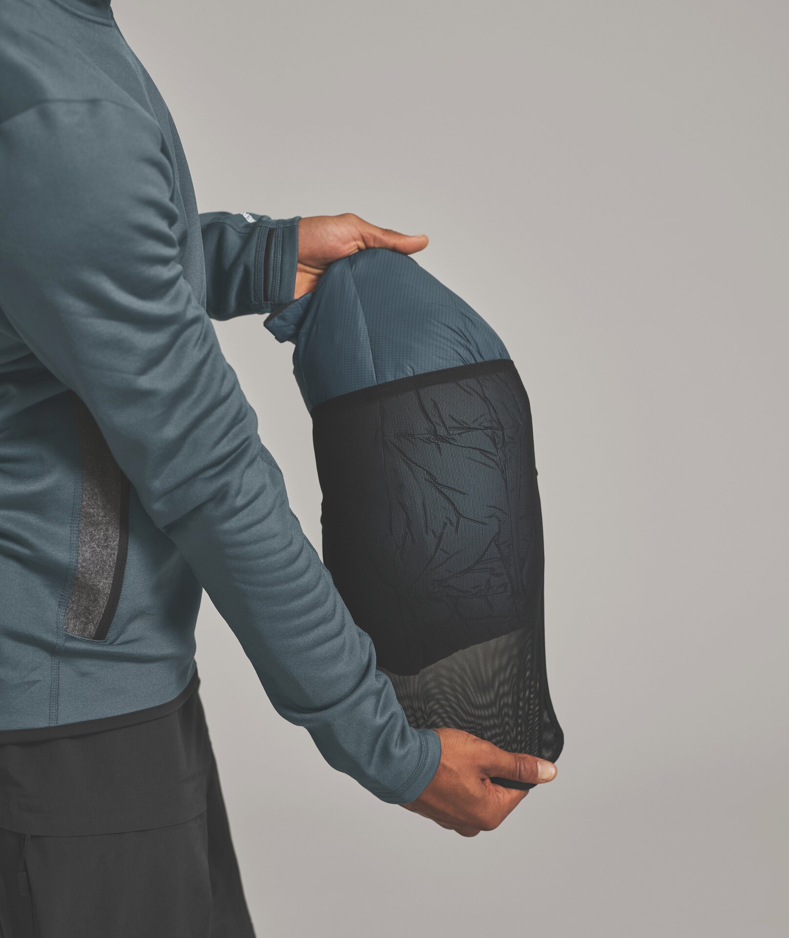 Person hält Schlafsack in einer schwarzen Netztasche vor hellgrauem Hintergrund.