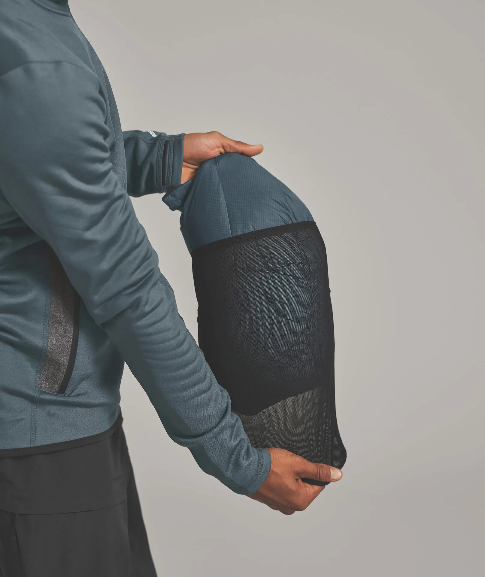 Person hält Schlafsack in einer schwarzen Netztasche vor hellgrauem Hintergrund.