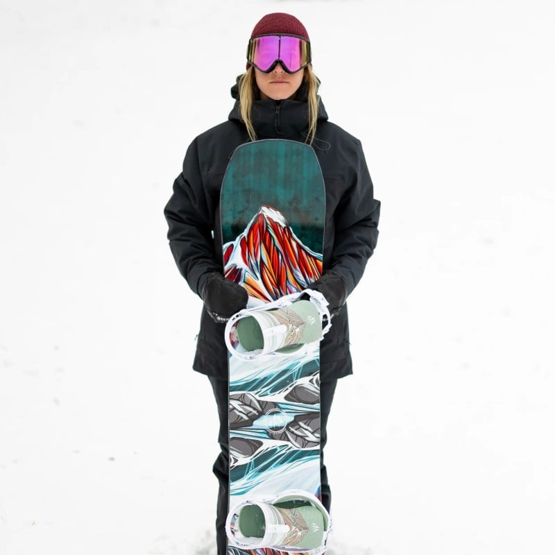 Twin Sister Snowboard Snowboarderin hält Twin Sister Snowboard mit Bergmotiv im Schnee.