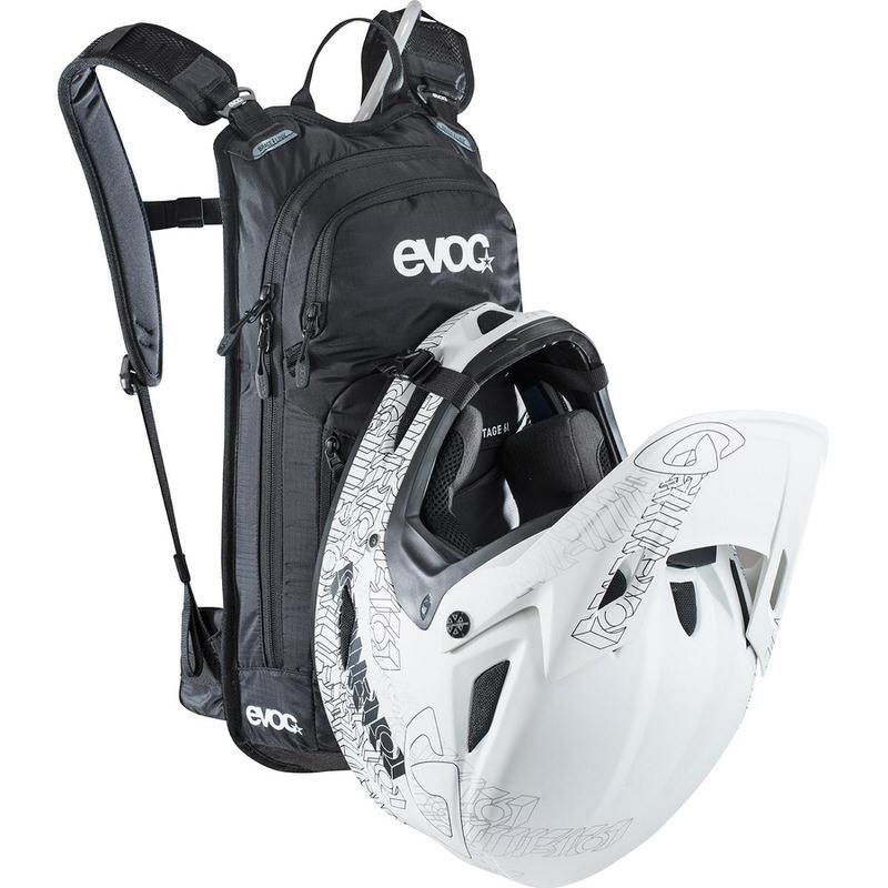Schwarzer Evoc Stage 6l Bikerucksack mit weißem Helm vor hellem Hintergrund.