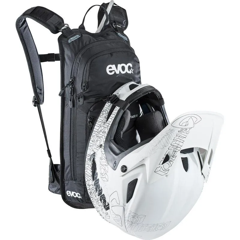 Schwarzer Evoc Stage 6l Bikerucksack mit weißem Helm vor hellem Hintergrund.