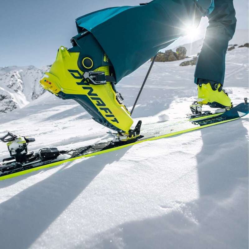 Gelber Dynafit Radical Pro Tourenskischuh auf Ski im Schnee, mit Skibindung. Person in Skikleidung, Sonnenschein.