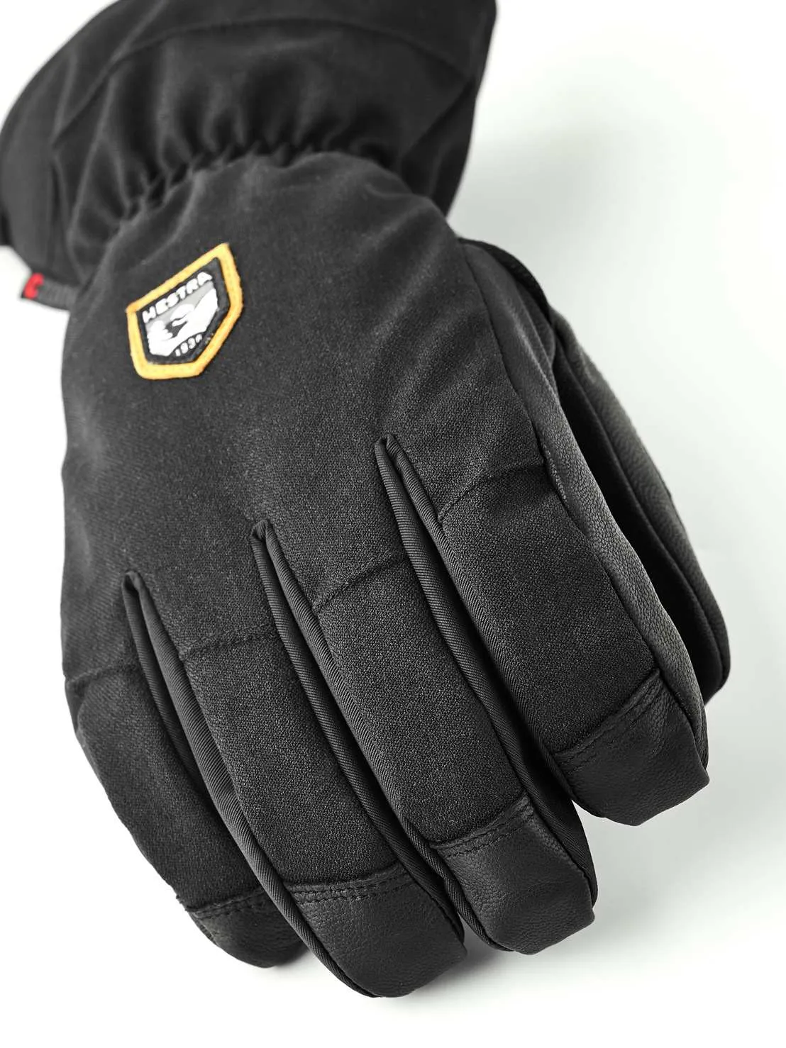 Nahaufnahme eines schwarzen Fünf-Finger-Handschuhs mit dem Hestra-Logo auf dem Handrücken.