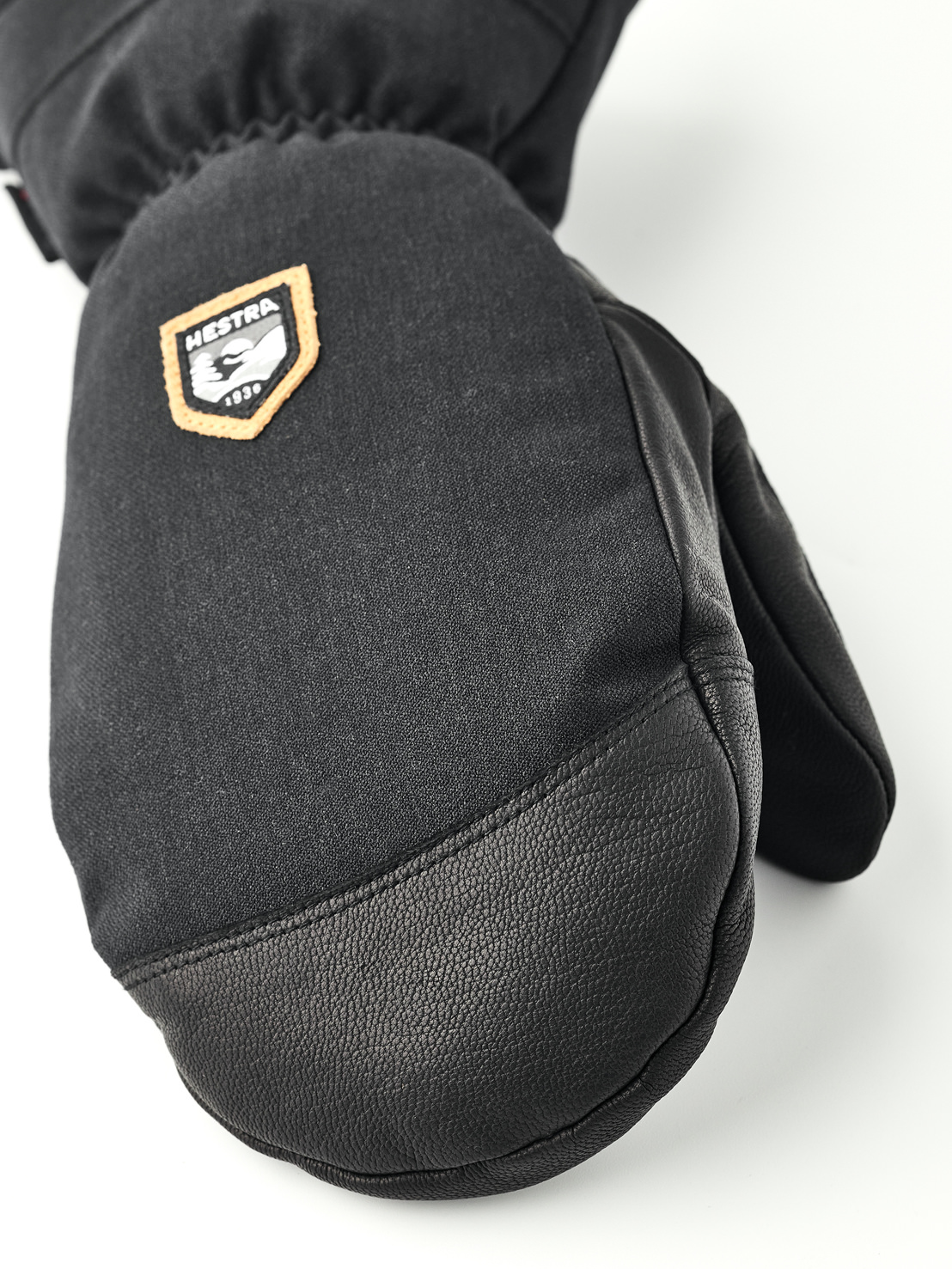 Black mitten Hestra Close-up of a black mitten made of fabric and leather with Hestra logo.