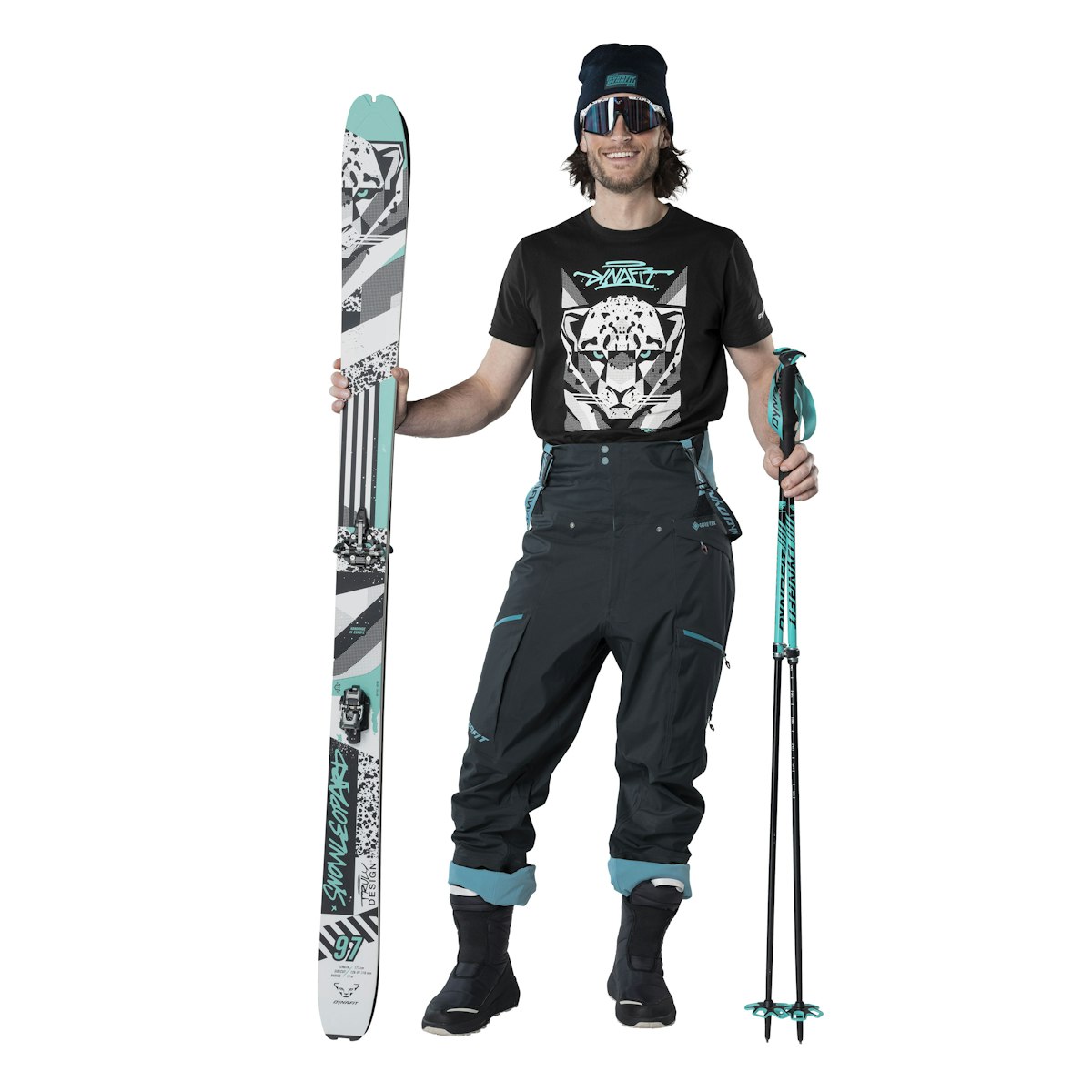 Leoparden-Skioutfit Skibekleidung: Mann mit Ski, Skistöcken, Mütze, Brille und T-Shirt mit Leopardenmotiv. Dunkle Skihose.