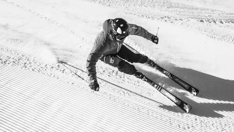 Foto in bianco e nero di uno sciatore in tenuta completa su una pista battuta.