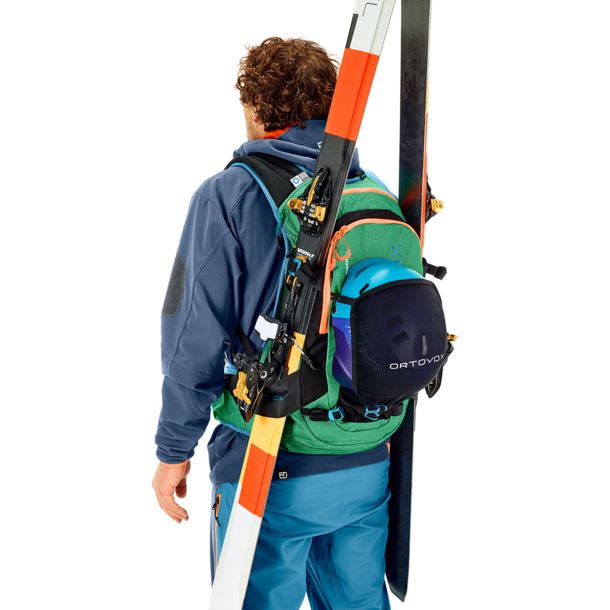 Eine Person trägt einen grünen Ortovox Free Rider 24 Rucksack mit Skiern und einem Helm darauf.