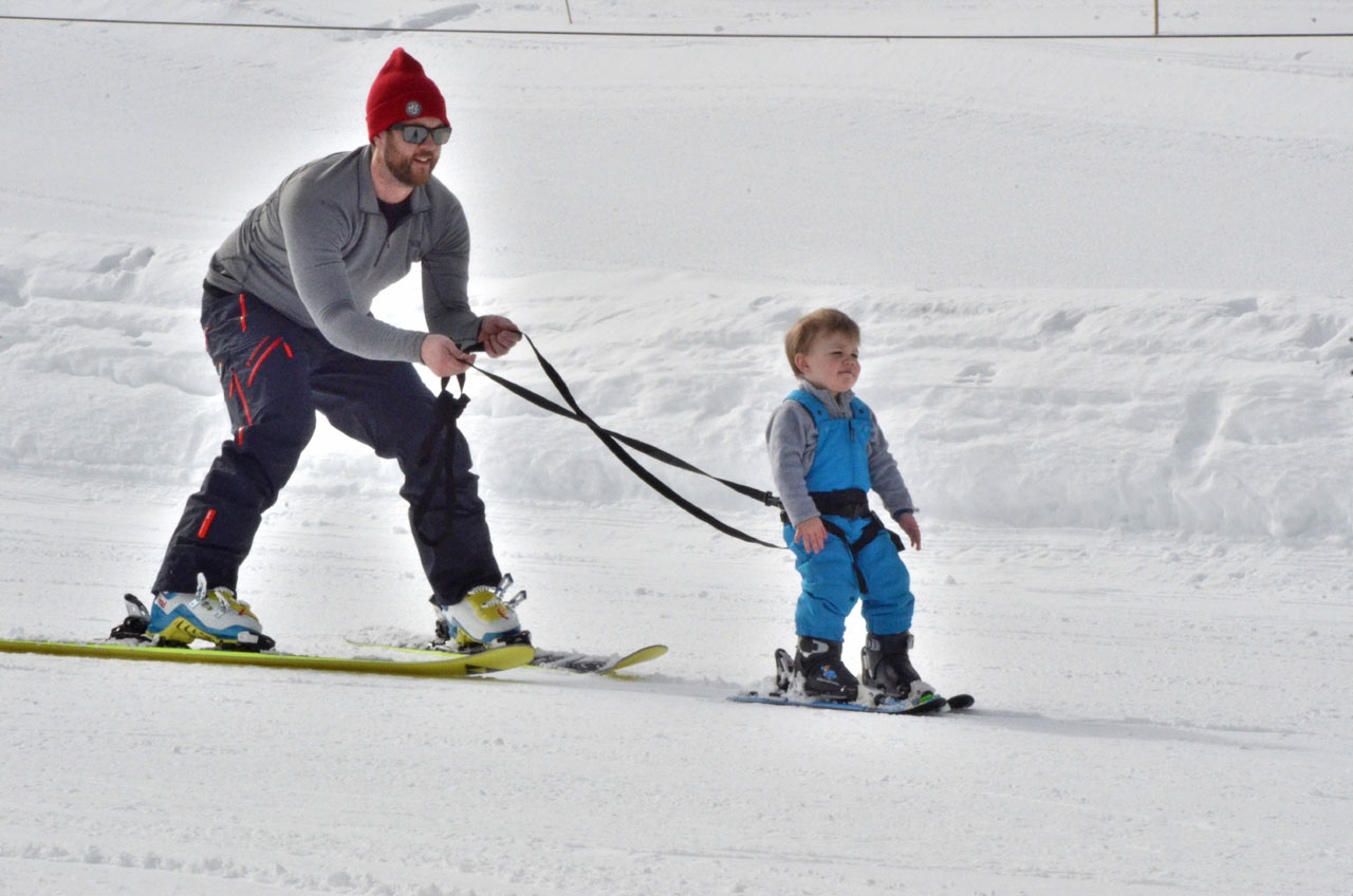 Vater zieht Kind mit SkiTies Ultimate Kid's Ski Harness auf Skiern im Schnee.