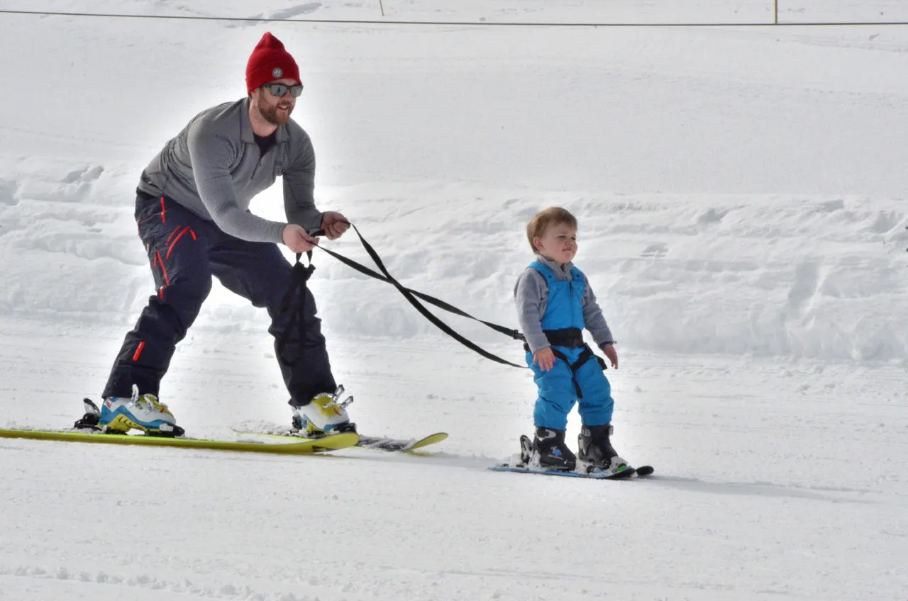 Father pulling child with SkiTies Ultimate Kid's Ski Harness on skis in the snow.
