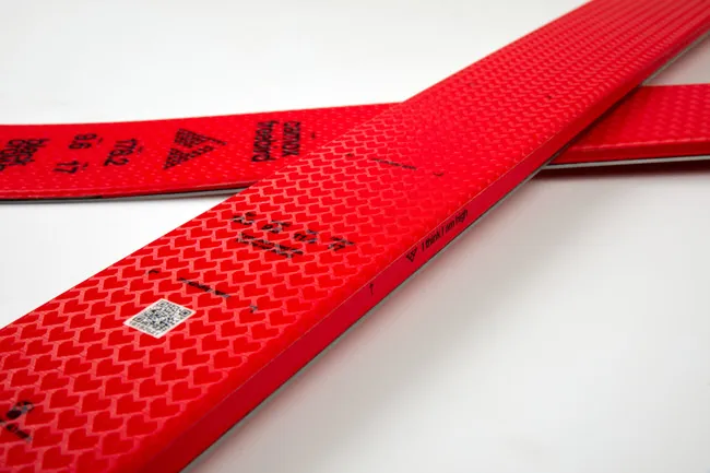Gros plan sur deux skis Black Crows Camox Freebird avec une surface rouge et un motif de petits cœurs. Texte et code QR visibles.