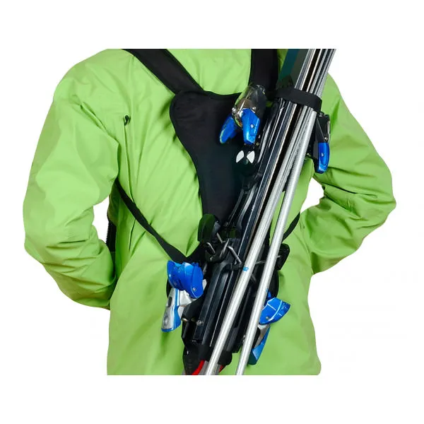 Person wearing a green anorak carries skis with a ski backpack like a rucksack.