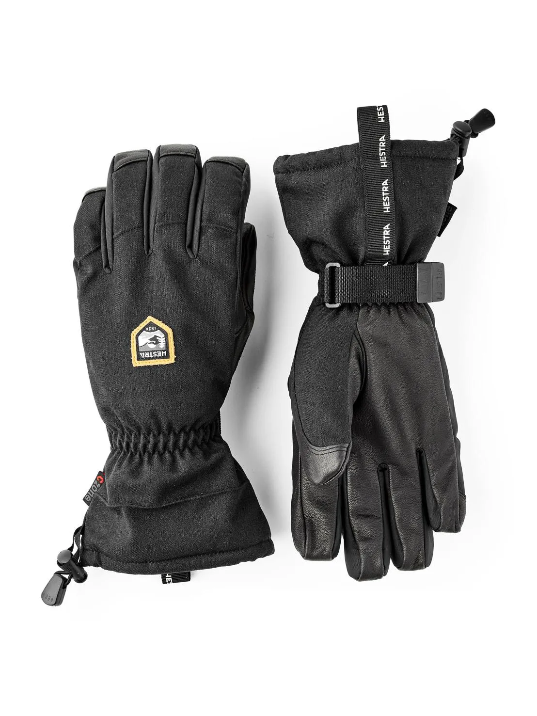 Zwei schwarze Hestra-Handschuhe, einer mit Stoffstulpe und Kordelzug, der andere mit Lederhandfläche und Gurtband.