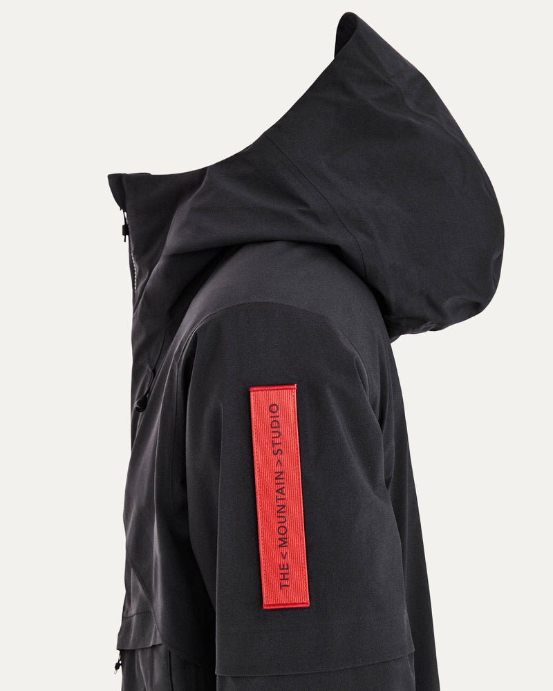 Schwarze S-1 Gore-Tex Jacke Nahaufnahme einer schwarzen S-1 Gore Tex Jacke mit Kapuze und rotem Logoaufnäher auf dem Ärmel.
