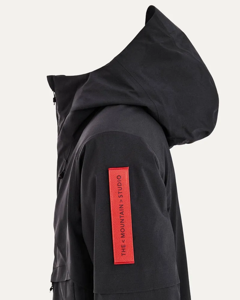 Nahaufnahme einer schwarzen S-1 Gore Tex Jacke mit Kapuze und rotem Logoaufnäher auf dem Ärmel.