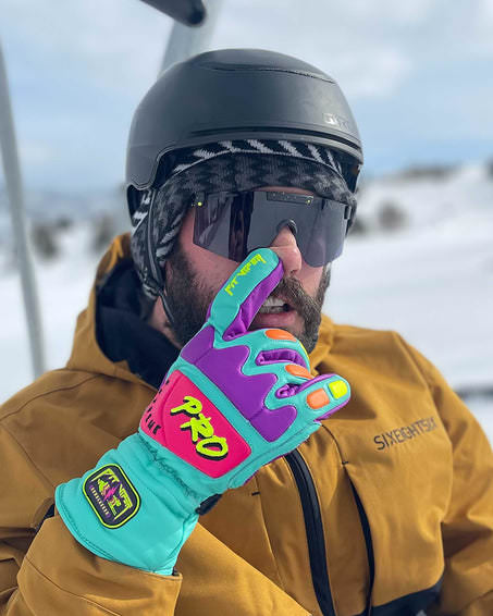 Mann mit Skihelm und Sonnenbrille, verdeckt Gesicht mit buntem Handschuh. `The Cosmos Photchromic 2000` Sonnenbrille sichtbar.