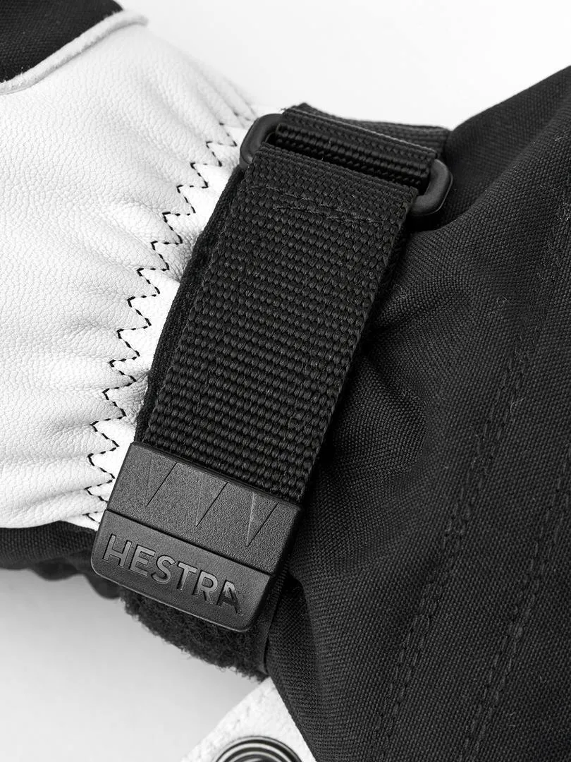 Détail d'un gant de ski noir Hestra avec une partie en cuir blanc et une sangle noire avec le logo Hestra.