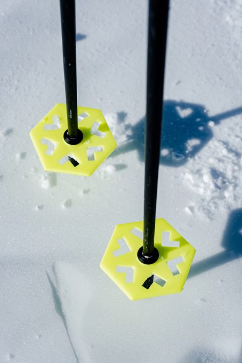 Zwei Black Crows Skistöcke im Schnee, gelbe Teller mit Aussparungen, Stöcke aus schwarzem Material.