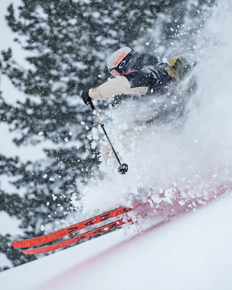Skieur avec des skis Van Deer dans la neige profonde, nuage de poussière et arbre en arrière-plan.