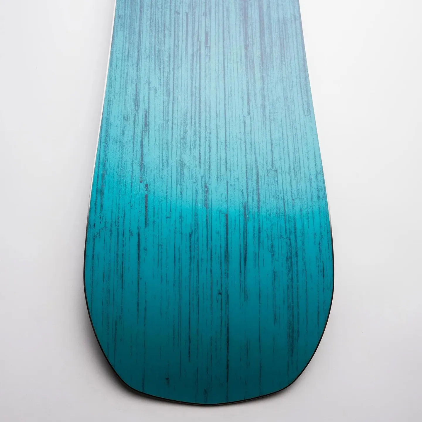 Detailansicht vom Nidecker Score Snowboard: Das Board hat ein blau-türkises Farbverlaufsmuster mit dunklen, vertikalen Linien.