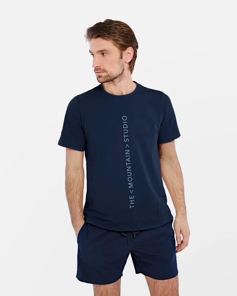 Man wears dark blue T-shirt with vertical "The Mountain Studio" logo and matching shorts.