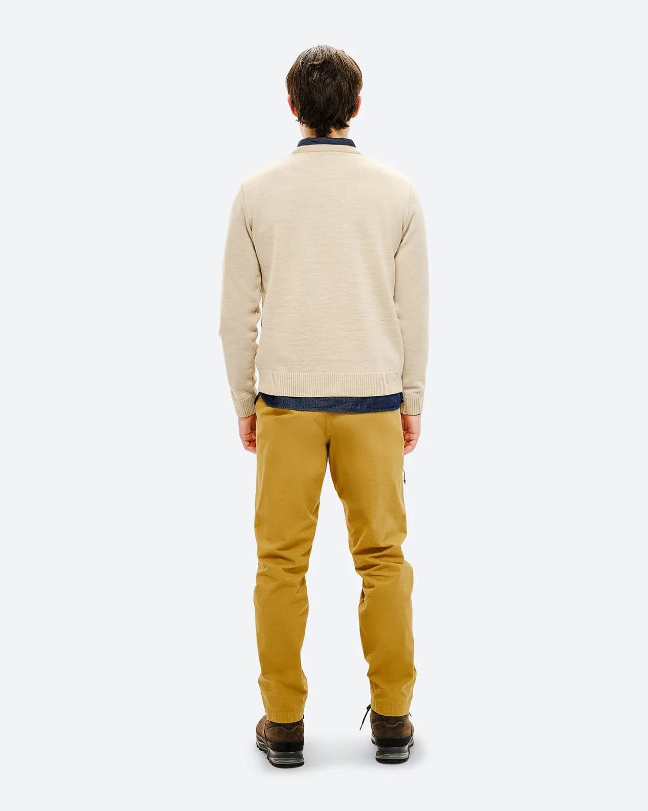 Vista posteriore di un uomo che indossa un maglione da sci beige, pantaloni gialli e scarpe marroni su uno sfondo neutro.