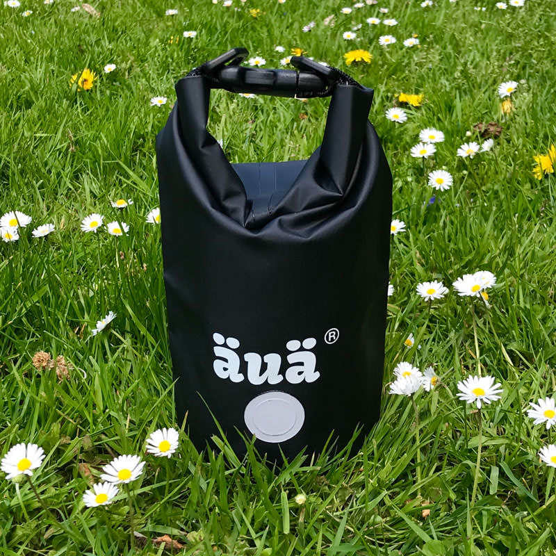 Dry Bag noir avec logo dans l'herbe, fermé par une poignée.