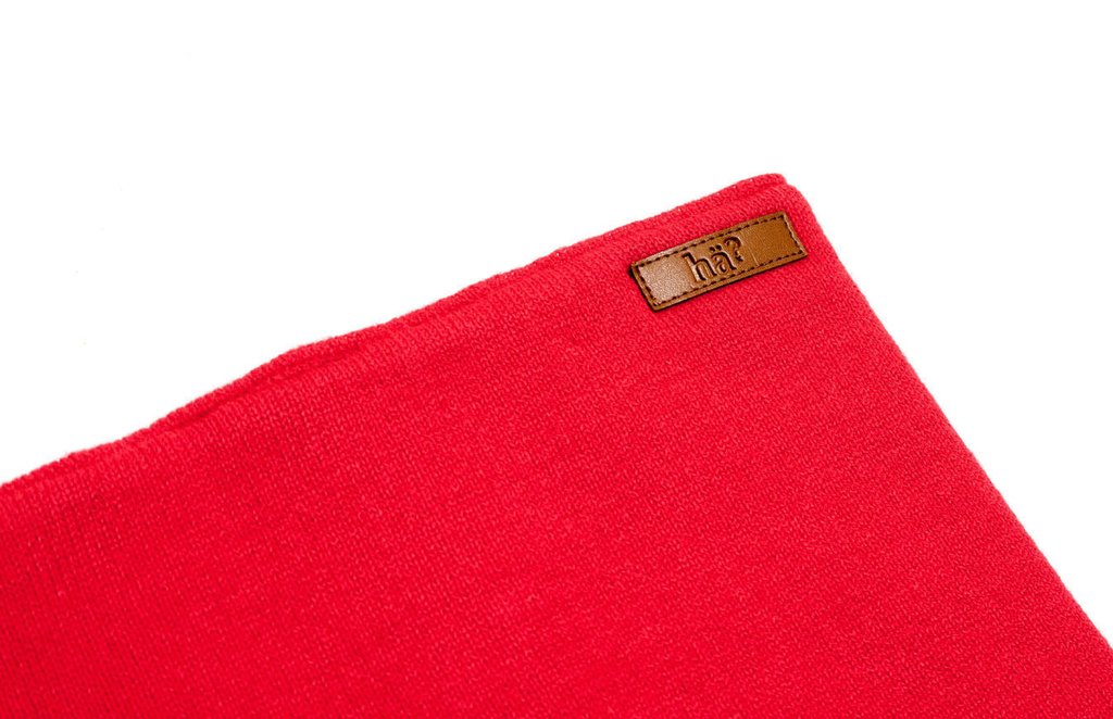 Roter, reversibler Neckwarmer mit Lederpatch. Nahe Aufnahme des roten Stoffes und Logo.