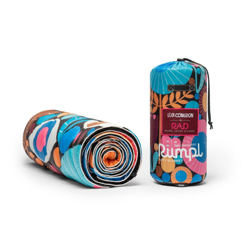Gerollte, farbenfrohe Rumpl Original Puffy Blanket Night Garden neben dem passenden Packsack.