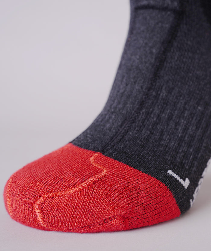 Nahaufnahme einer grauen Socke mit roter Spitze und verstärktem Bereich an der Fußsohle. Strickmuster sind sichtbar.