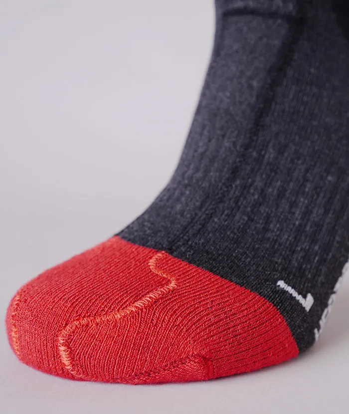 Gros plan sur une chaussette grise avec une pointe rouge et une zone renforcée sur la plante du pied. Les motifs de tricot sont visibles.