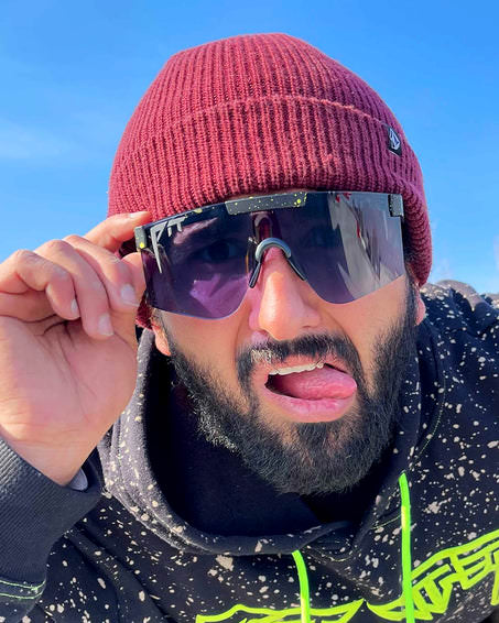 Mann mit Mütze und 'Cosmos Photchromic 2000' Sonnenbrille mit Zunge raus, trägt einen Hoodie mit neonfarbenen Details.