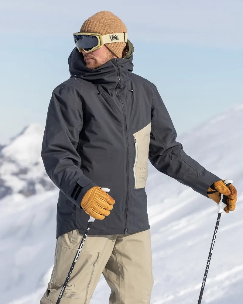 Man with ski goggles and cap wearing gray Ride Insulated Jacket and gloves, holding ski poles in the snow.