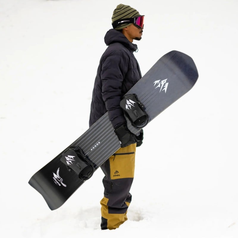 Freecarver 9000s Snowboard Person hält Freecarver 9000s Snowboard im Schnee, trägt Mütze und Skibrille.