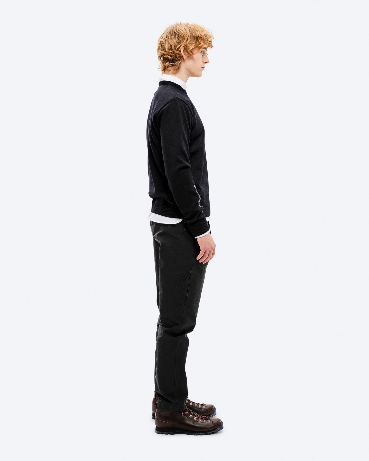 Male skiLook A man in profile wears a black merino wool K-3 ski sweater, dark pants and brown hiking boots.