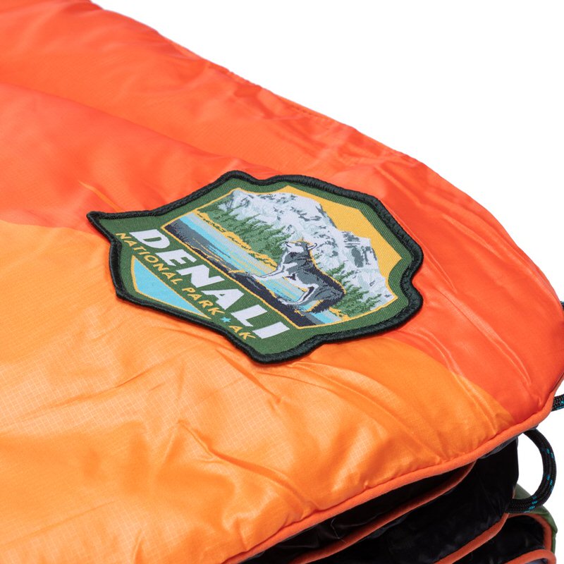 Nahaufnahme der Rumpl Original Puffy Decke mit Denali National Park Logo auf orangefarbenem Stoff.