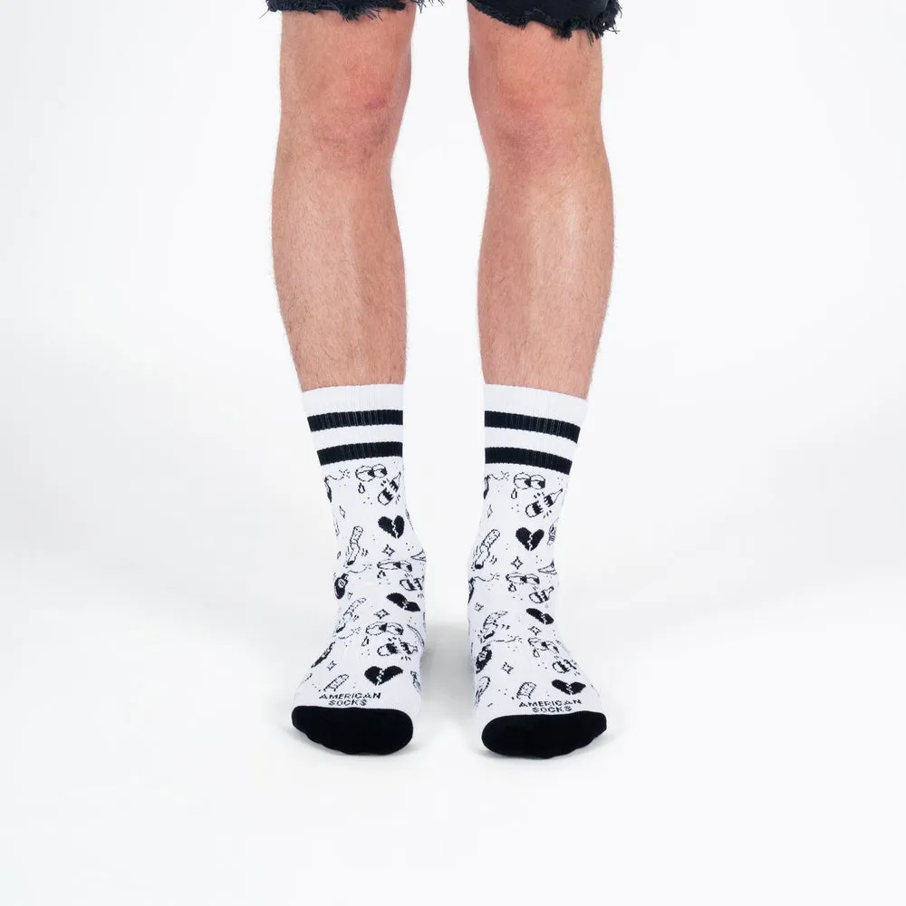 Legs with white, medium-high socks, decorated with black tattoo motifs and stripes on the upper edge.