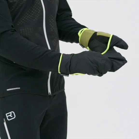 Una persona indossa i guanti Ortovox Fleece Grid Cover nei colori nero e verde. Il cappuccio di copertura è tirato sulle dita.