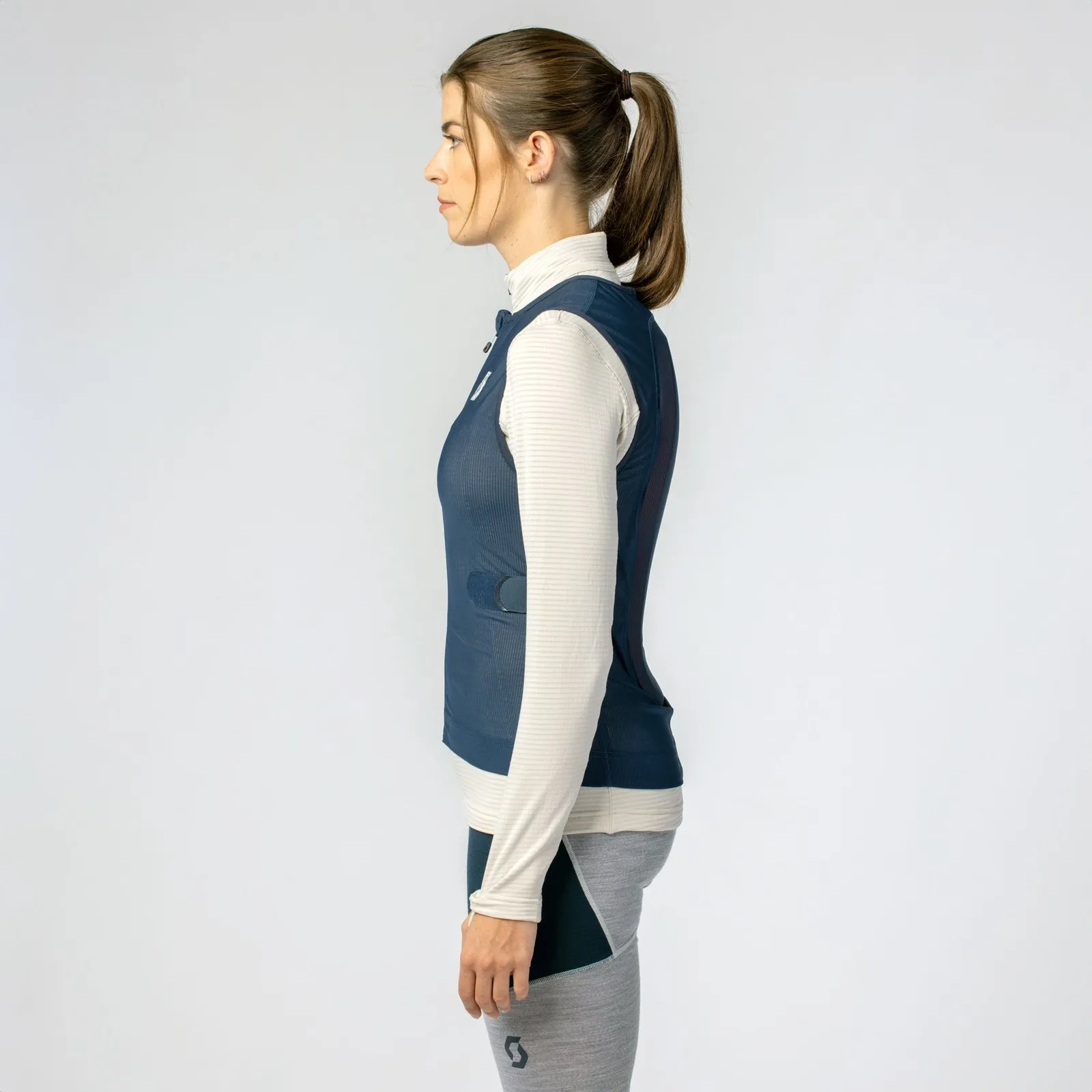 Profile view of a woman wearing a black/white Scott Airflow vest over a long-sleeved top.