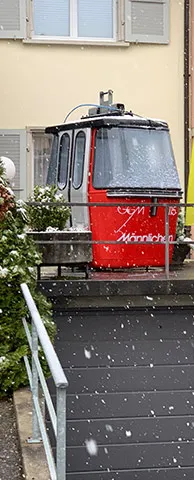 Eine rote Gondel "Männlichen" steht vor einem Haus bei leichtem Schneefall.