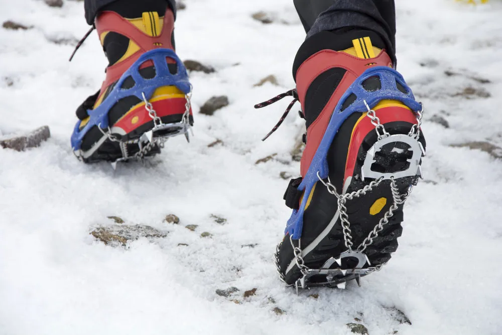 Nahaufnahme: Trekking-Schuhe mit montierten Steigeisen auf Schnee, mit Ketten und Stahlplatten für verbesserten Halt.