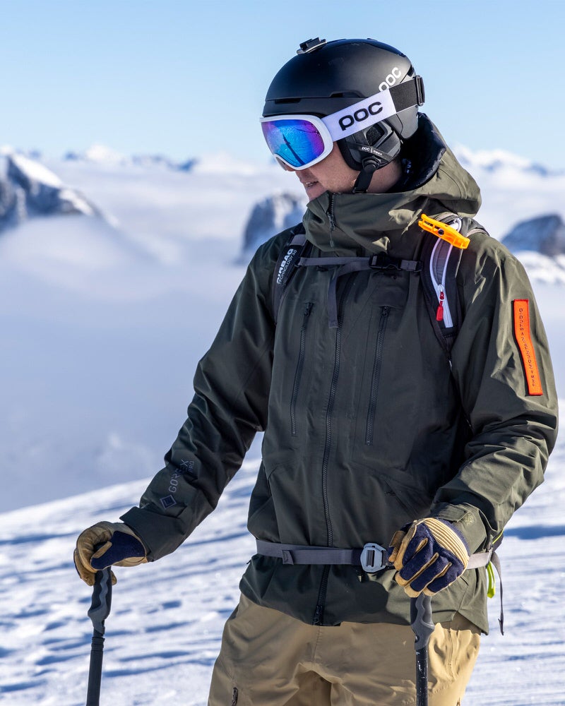 Skifahrer in GORE-TEX Jacke Skifahrer in grüner Z-2 HD GORE-TEX Pro Jacke vor verschneiter Bergkulisse.