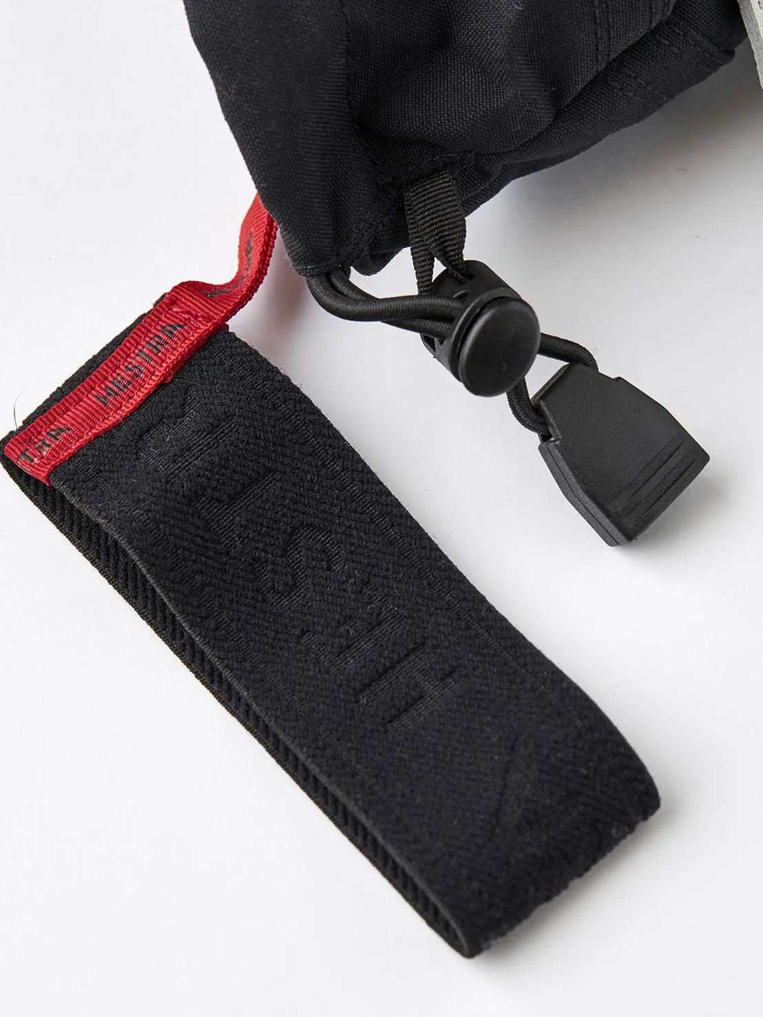 Nahaufnahme eines schwarzen Handschuhs mit roter Schlaufe und schwarzem Gummizug mit Verschluss vor weißem Hintergrund.