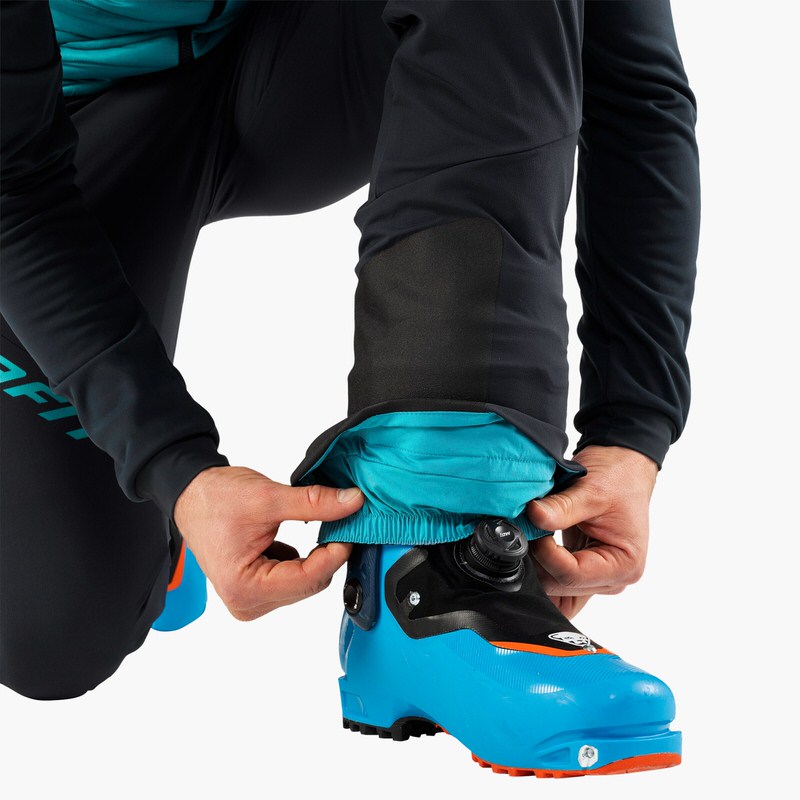 Person justiert TLT Touring DST Hose über Skischuh, Farbe Blueberry/Marine Blue.