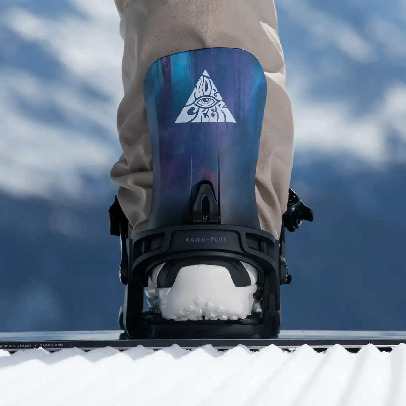 Close-up of a snowboard with bindings and boots, seen from behind with blue background.