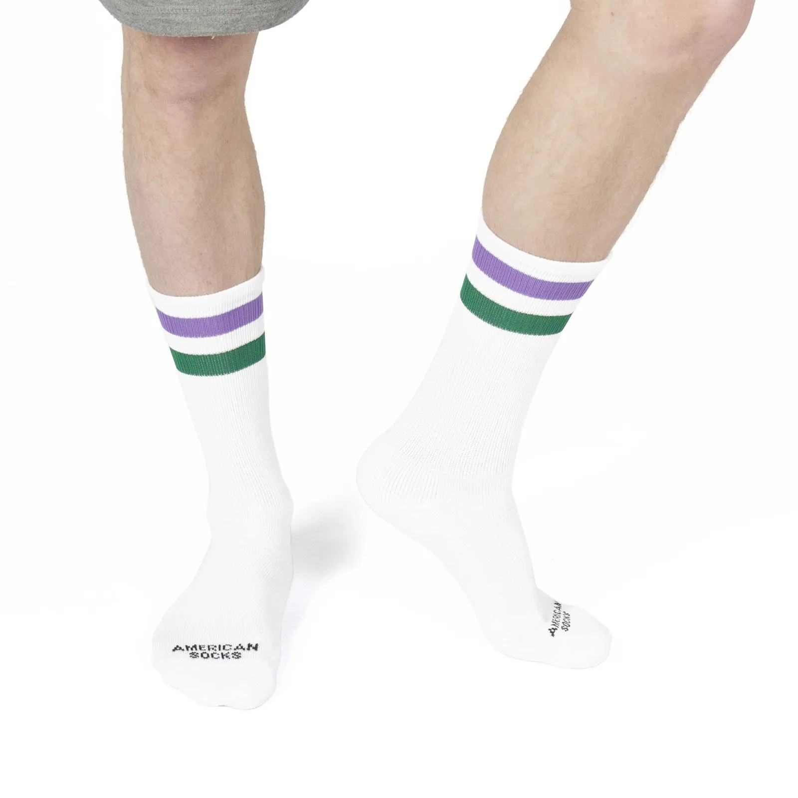Beine mit weißen Mid High Socken. Streifen in Lila und Grün am Bündchen. Logo "American Socks" ist zu sehen.