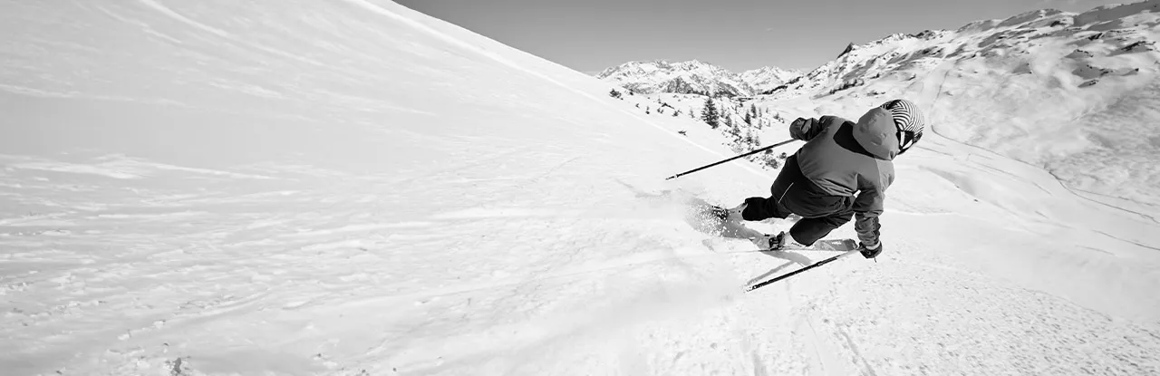Black and white photograph of a person skiing on a snowy slope, with mountains in the background.