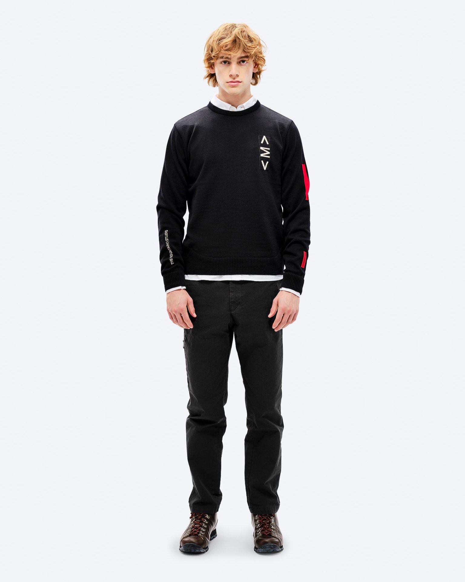 Man in K-3 ski sweatshirt Man with red hair wearing black K-3 ski sweater with red accents and black pants, posing in front of a white background.