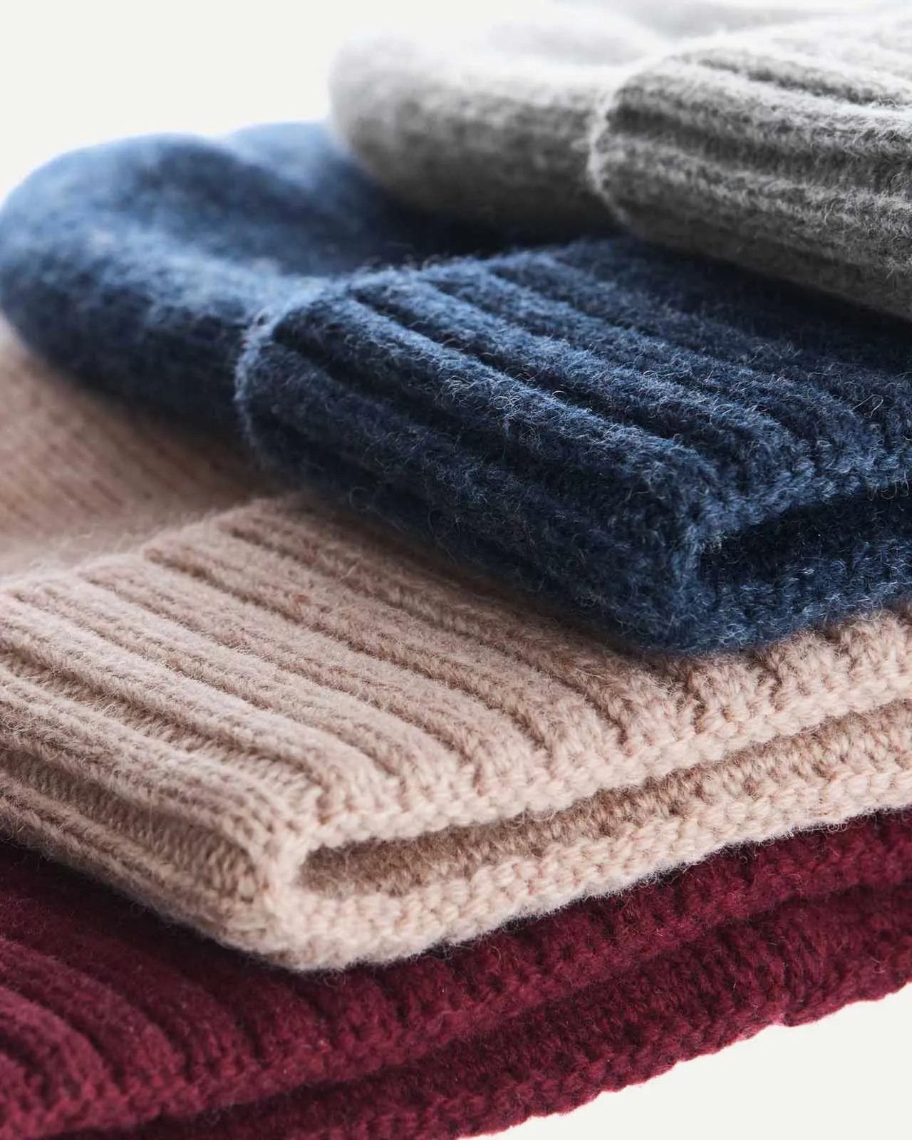 Close-up of a stack of several cashmere mix beanies in red, beige, blue and gray.