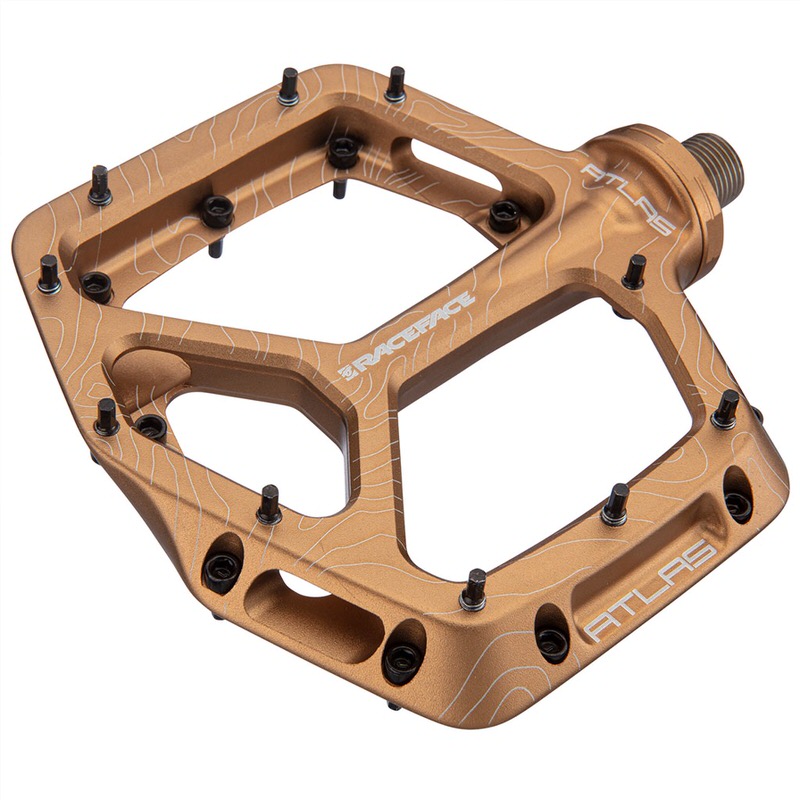 Goldenes Race Face Atlas V2 Pedal mit schwarzen Pins und eingraviertem Logo auf weißem Hintergrund.